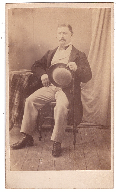Homme assis tenant son chapeau et sa canne.