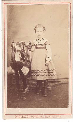 Petite fille debout près d'une chaise où elle a posé son chapeau