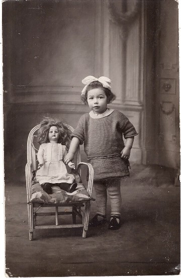 Fillette posant près de sa poupée qu'elle a assise dans un fauteuil