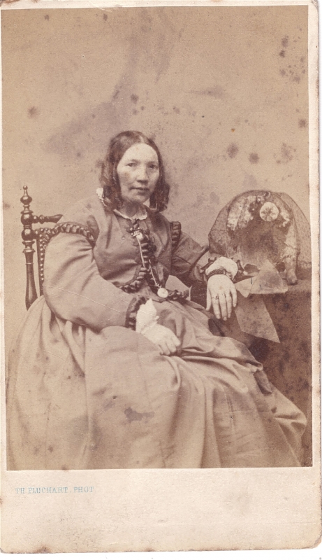 Femme assise près d'une table sur laquelle est posé un objet non identifié : couronne de mariée  sous un voile (?)