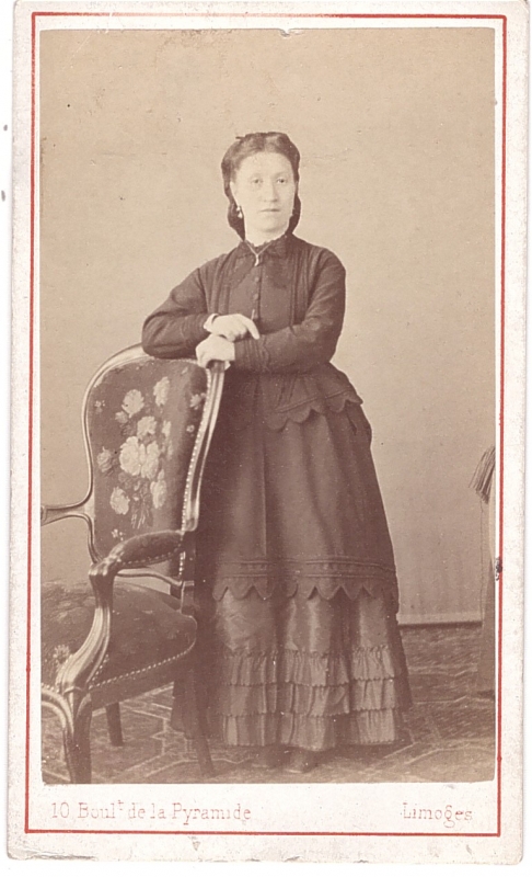Femme posant debout, les mains posées sur le dossier d'un fauteuil