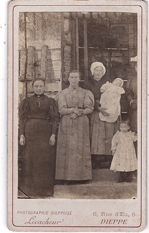 Trois femmes dont l'une tient un nouveau-né posant devant leur commerce.