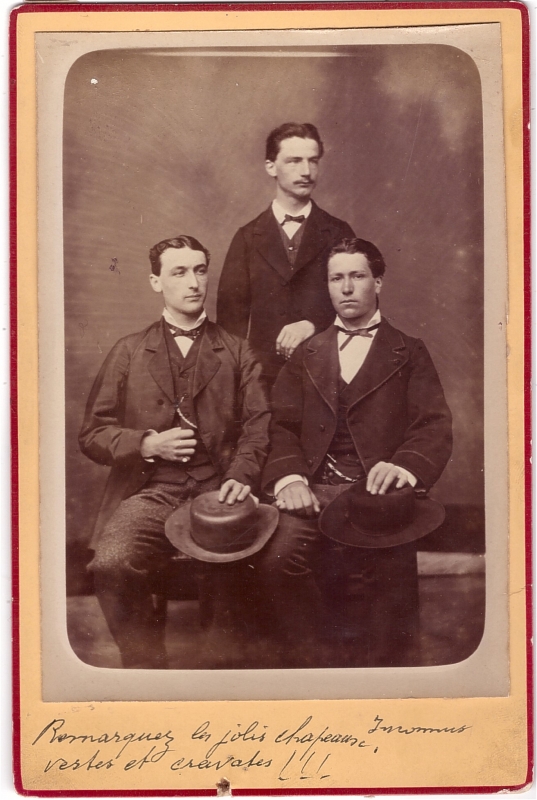 Trois hommes dont deux assis leur chapeau sur les genoux