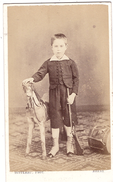 Garçonnet, tenant une carabine, qui pose près d'un cheval de bois