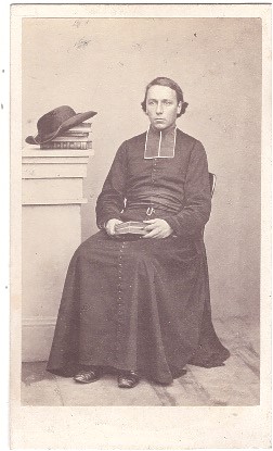 L'abbé Buisson posant assis, son chapeau posé sur une pile de livres
