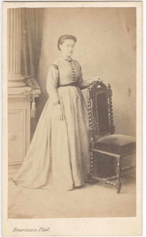 Femme debout, une main posée sur le dossier d'une chaise