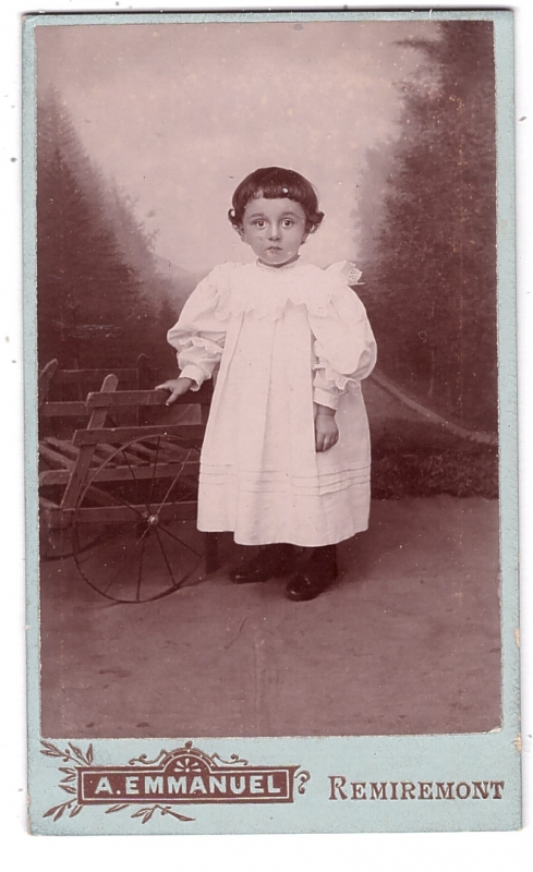 Bambin en robe blanche posant à côté d'une petite charrette