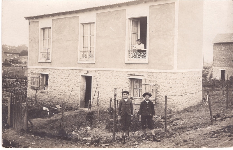 Deux garçons devant une maison avec une femme à sa fenêtre