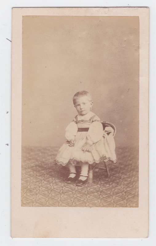 Enfant en robe blanche assis sur une chaise