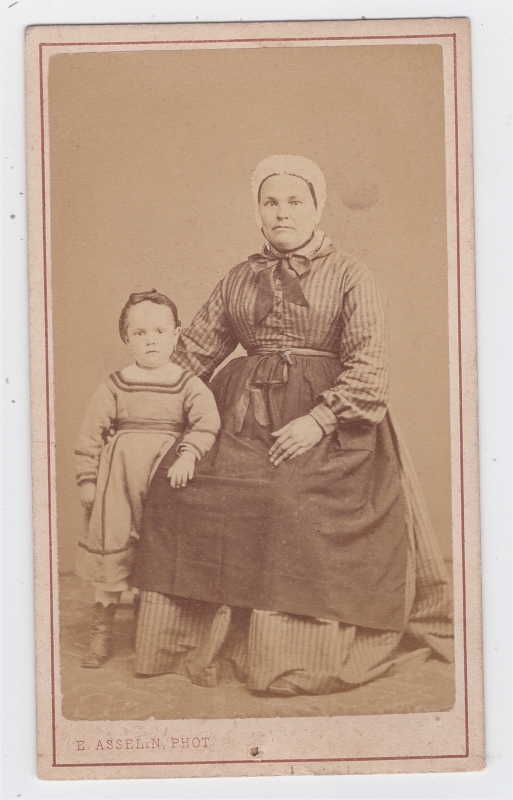 Femme portat un tablier sur sa robe, posant avec son enfant 